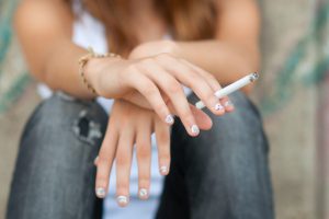 Teenage hands holding cigarette outdoor.