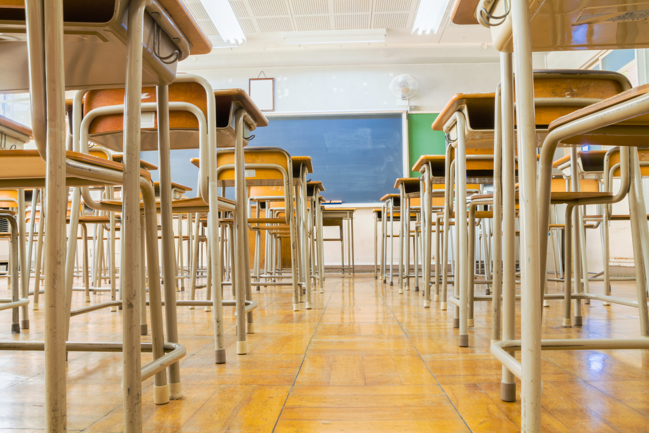 A Japanese classroom with desk and tables and blakckboard is taken from low angle.